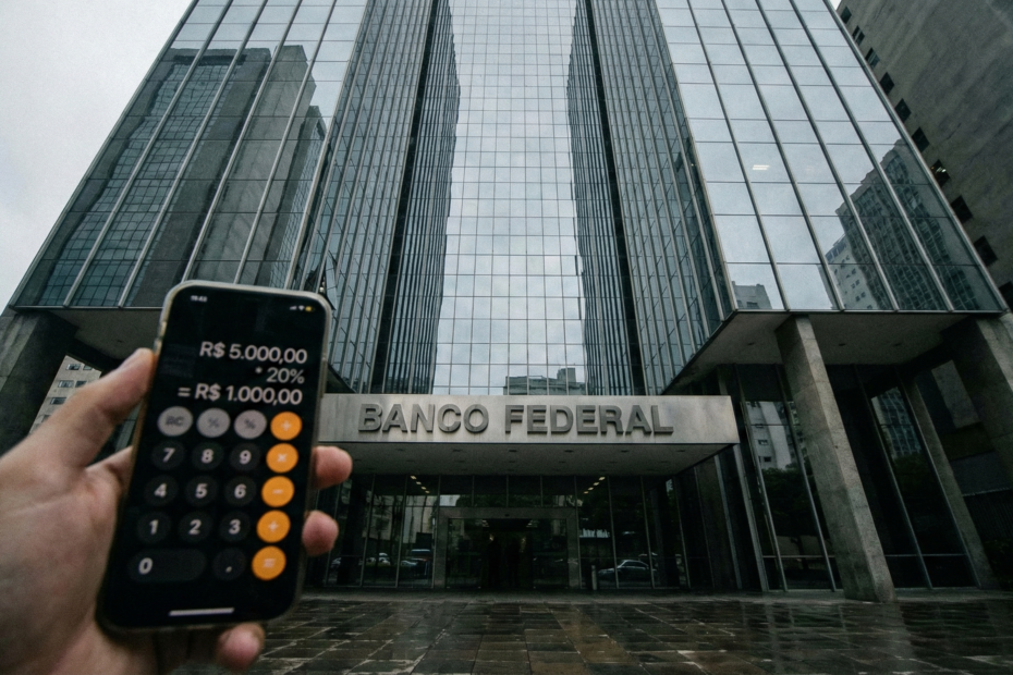 Fachada de banco moderno vista de baixo com calculadora em primeiro plano simbolizando o cálculo de juros.